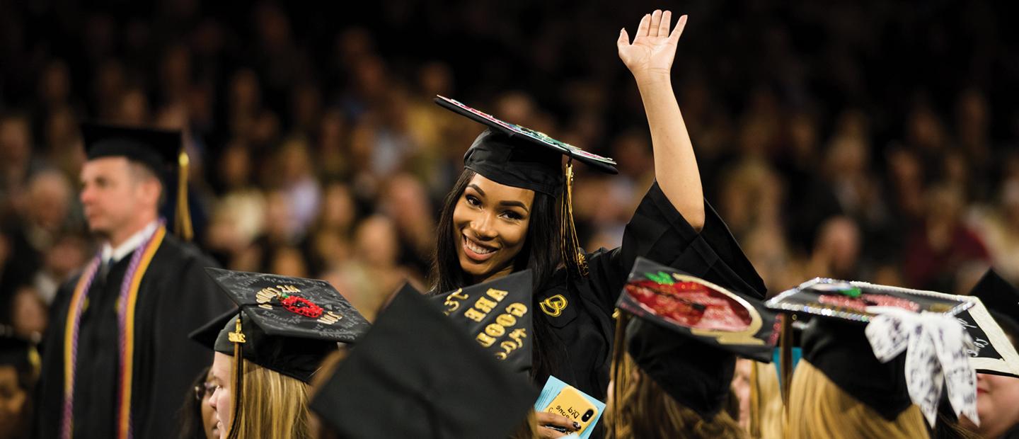 Banner with a woman in here graduation outfit smiling and waving surrounded by other graduates.